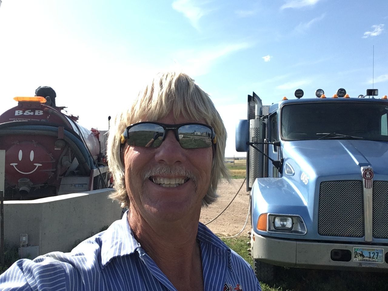 Smiling person in sunglasses standing between two trucks on a sunny roadside. Smiling person in sunglasses standing between two trucks on a sunny roadside.