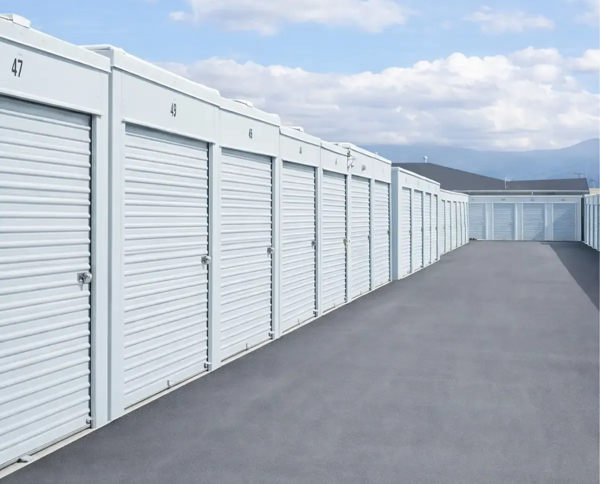 Row of white storage unit doors beside a paved lane under a cloudy sky
