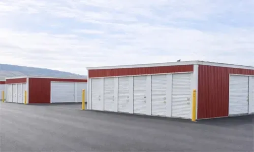 Row of red and white storage units with closed garage doors on a paved lot