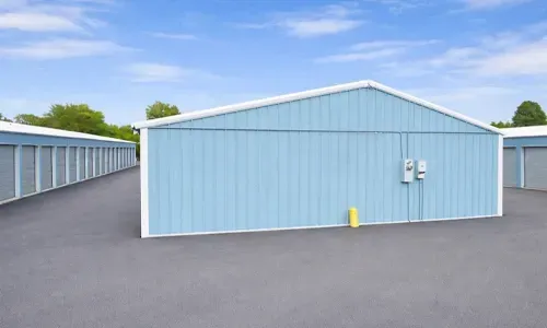 Light blue storage building with white trim in a paved lot, flanked by rows of similar units