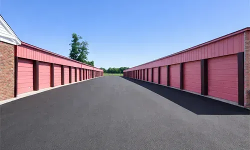 Row of red storage units lining a wide paved lane under a clear blue sky