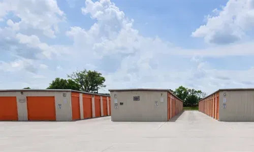 Row of orange storage units with a central gray building under a partly cloudy sky