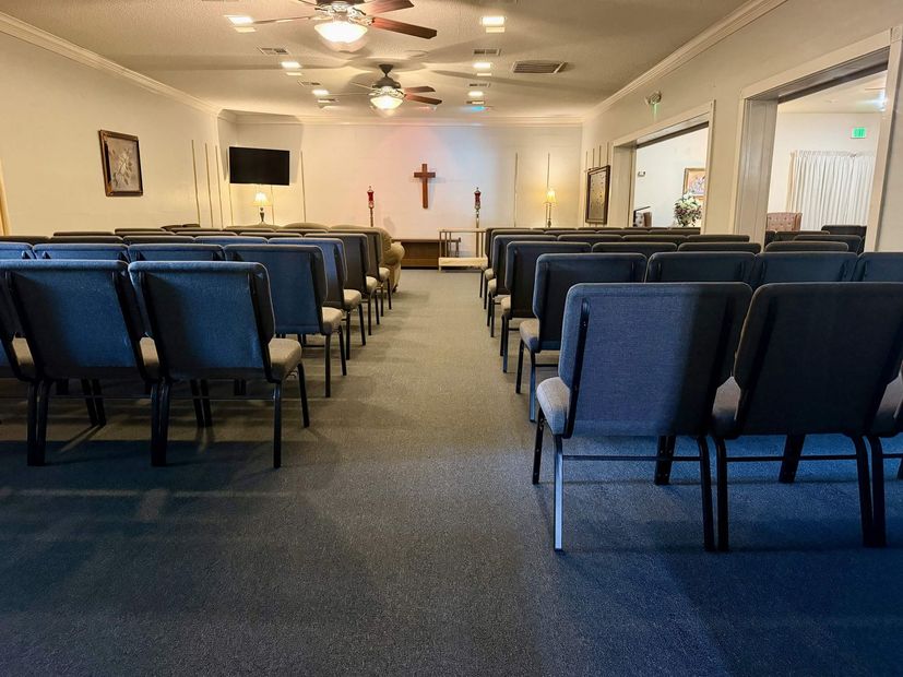Empty church sanctuary with blue pews, ceiling fans, and a cross at the front.