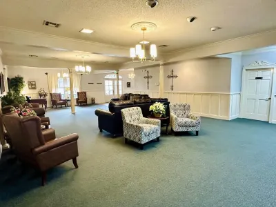 Spacious lobby with teal carpet, patterned armchairs, and warm ceiling lights in a beige room