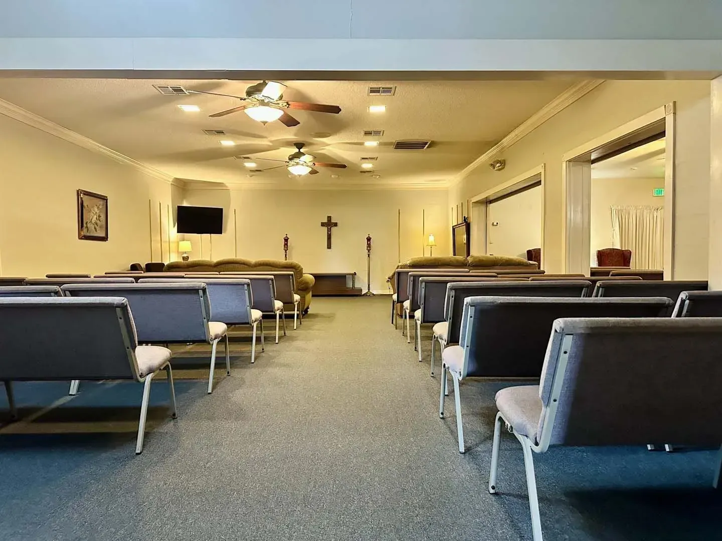 Empty church sanctuary with blue pews, ceiling fans, and a cross at the front.