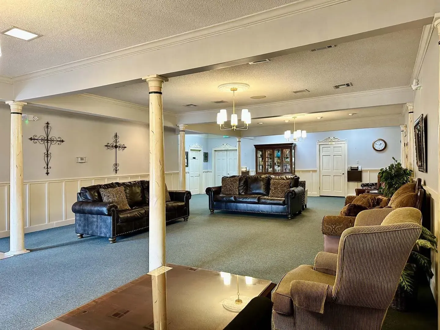 Spacious living room with blue carpet, leather sofas, columns, and a ceiling light fixture