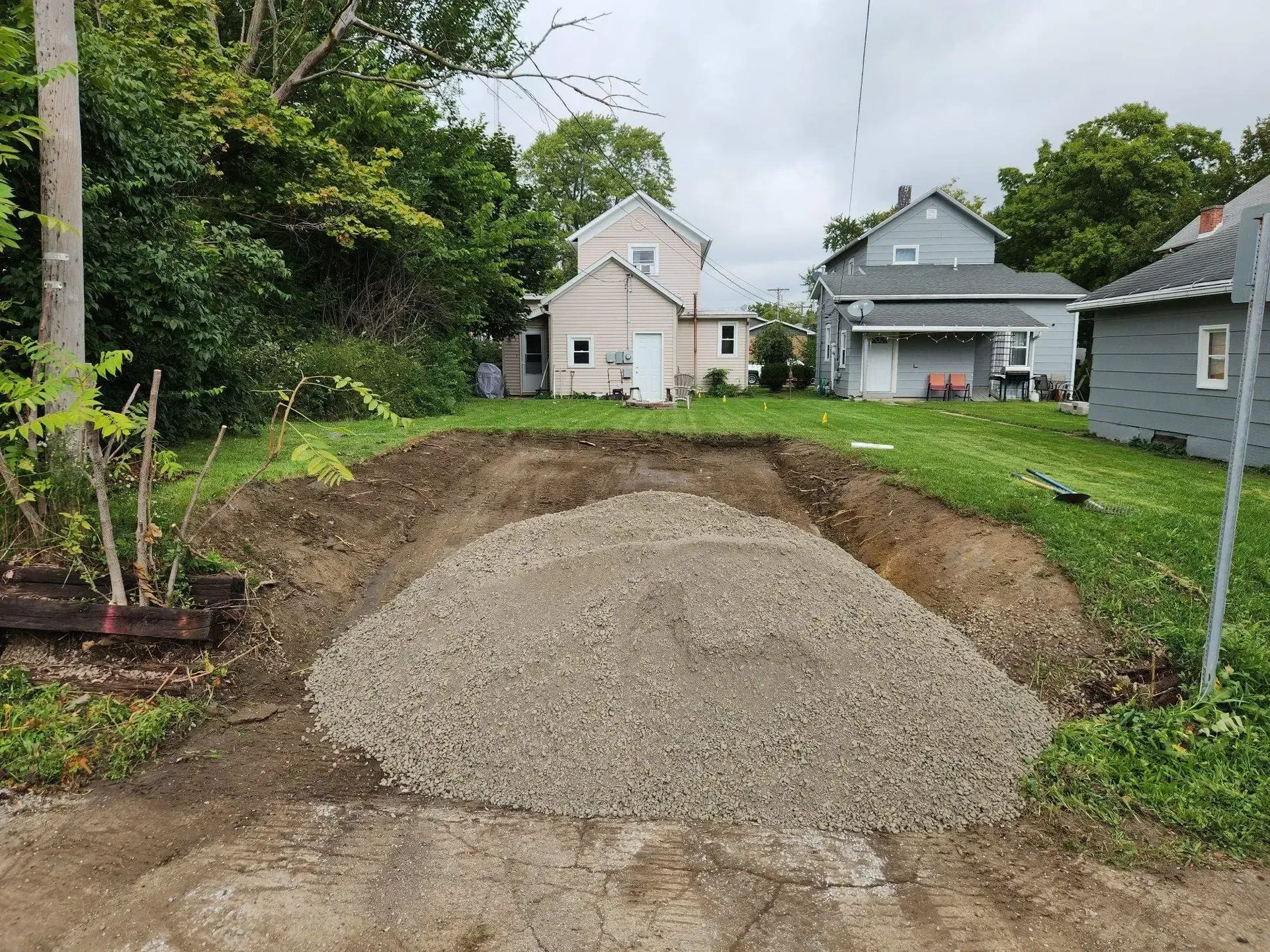 Fresh gravel pile in a dug-out front yard with houses and a lawn in the background