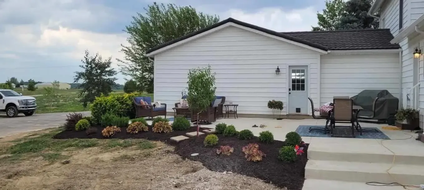 Suburban house with white siding, front porch chairs, and landscaped flower beds by a driveway