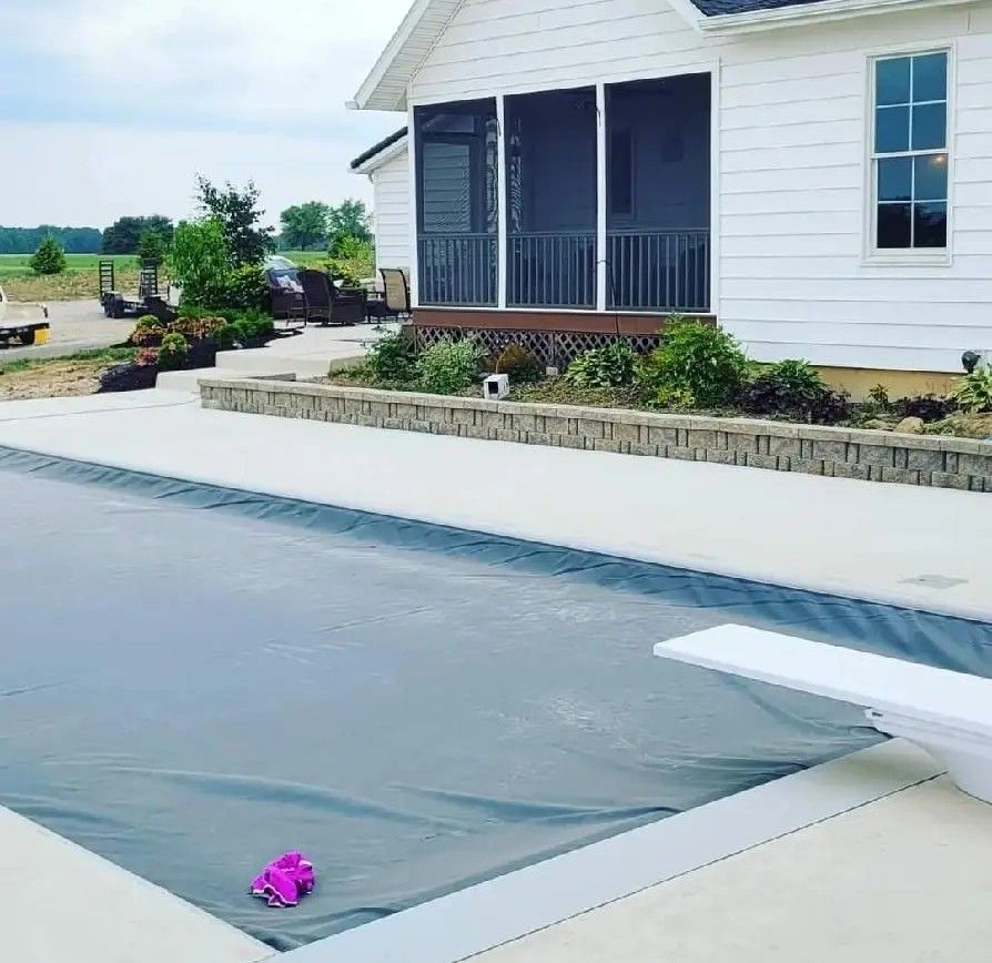 Covered backyard pool under construction beside a white house, with dark liner and concrete patio.