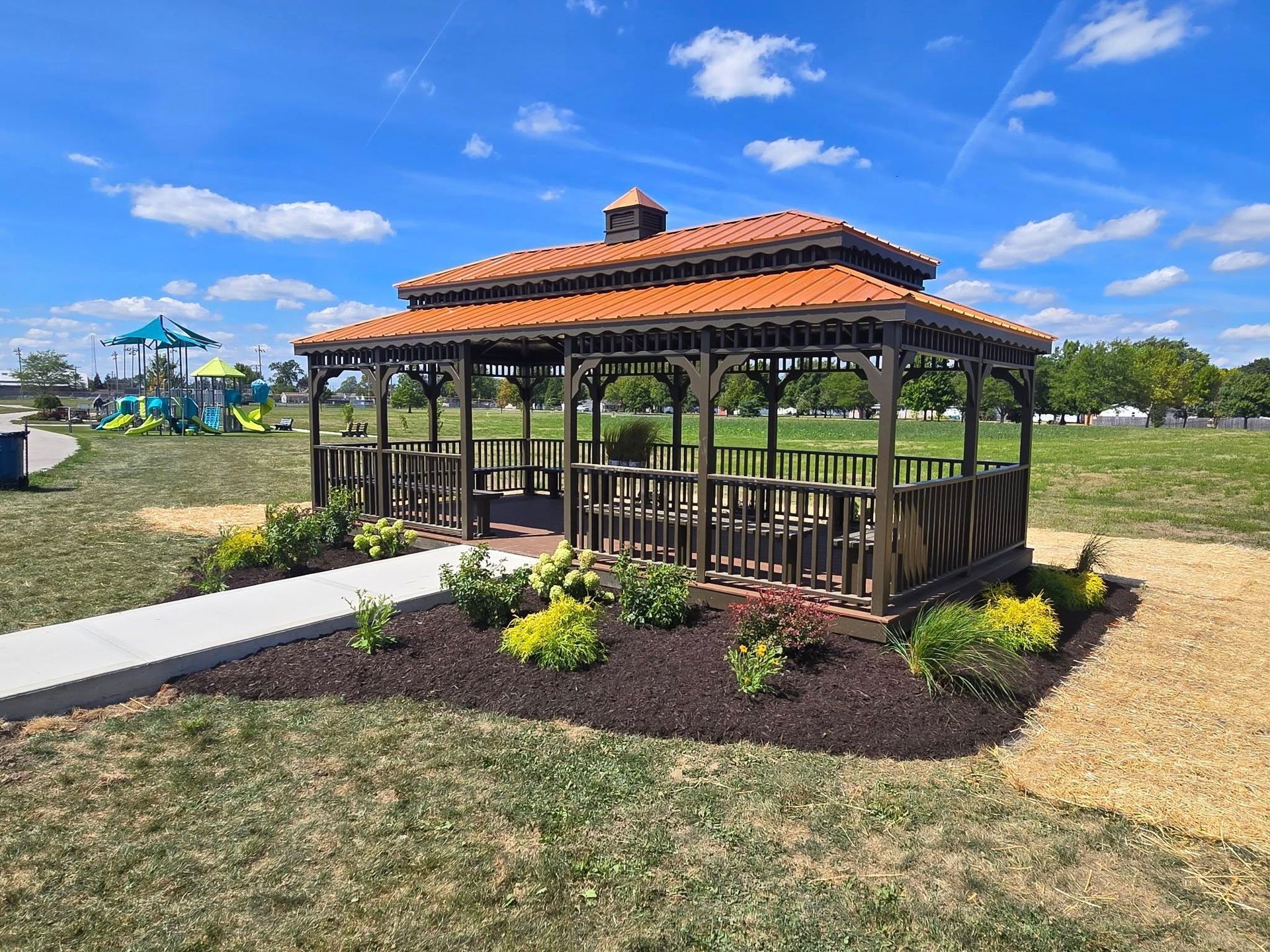 Gazebo with red-tile roof in a landscaped park under a bright blue sky