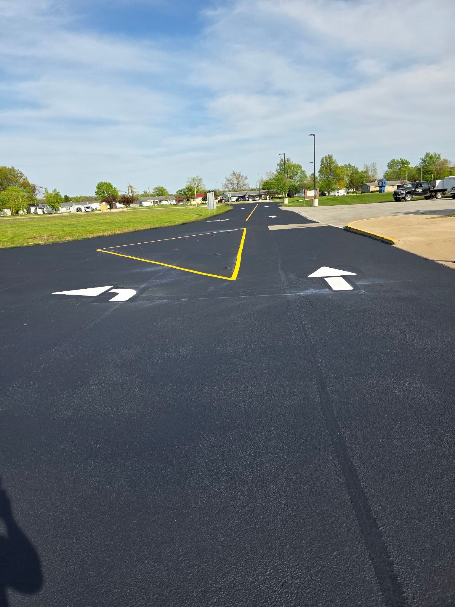 Empty paved lot with white arrows and a dashed yellow line under a clear sky.