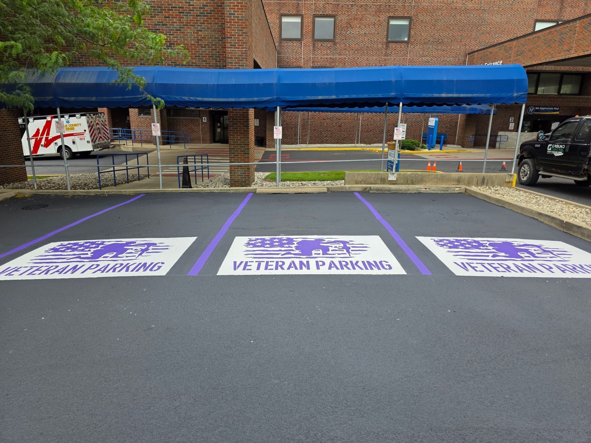 Veteran parking spaces painted in purple and white under a blue canopy near a brick building.