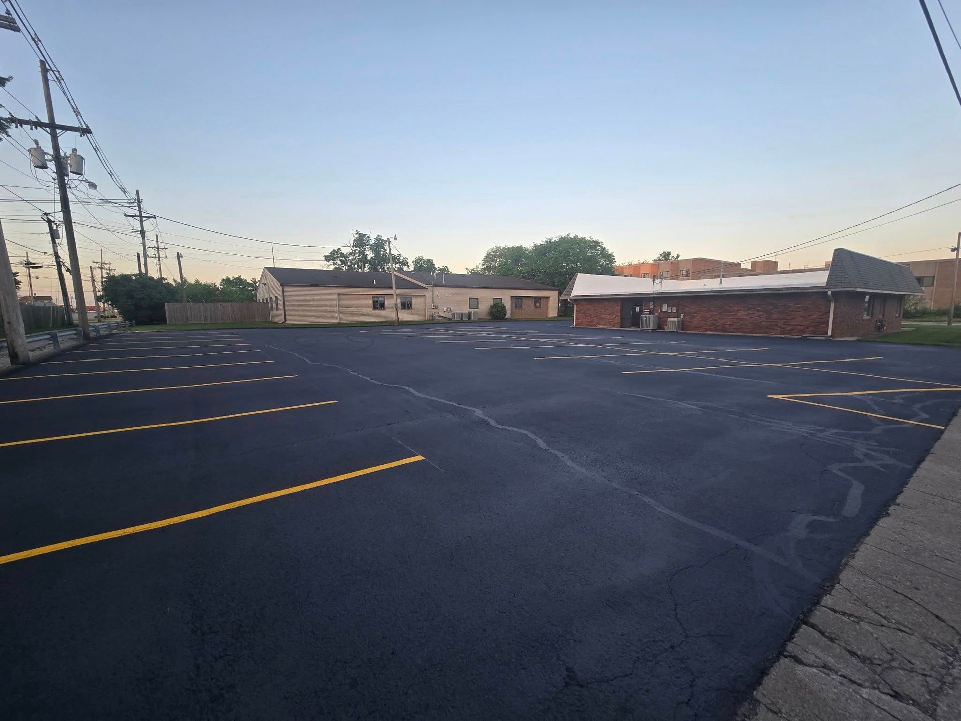 Empty paved parking lot at dusk with yellow parking lines and low buildings in the background