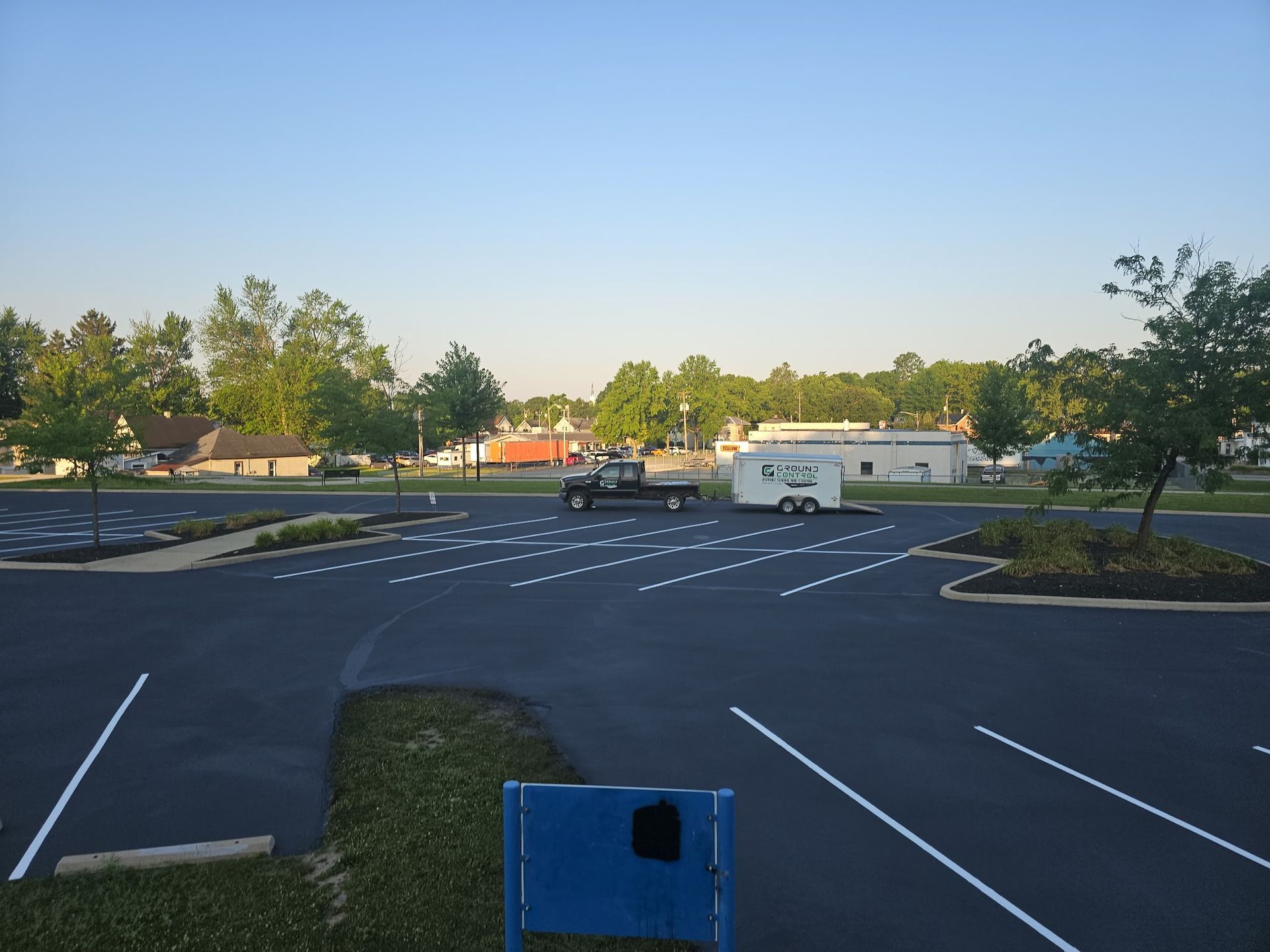 Empty parking lot at dusk with a white van, trees, and a clear blue sky