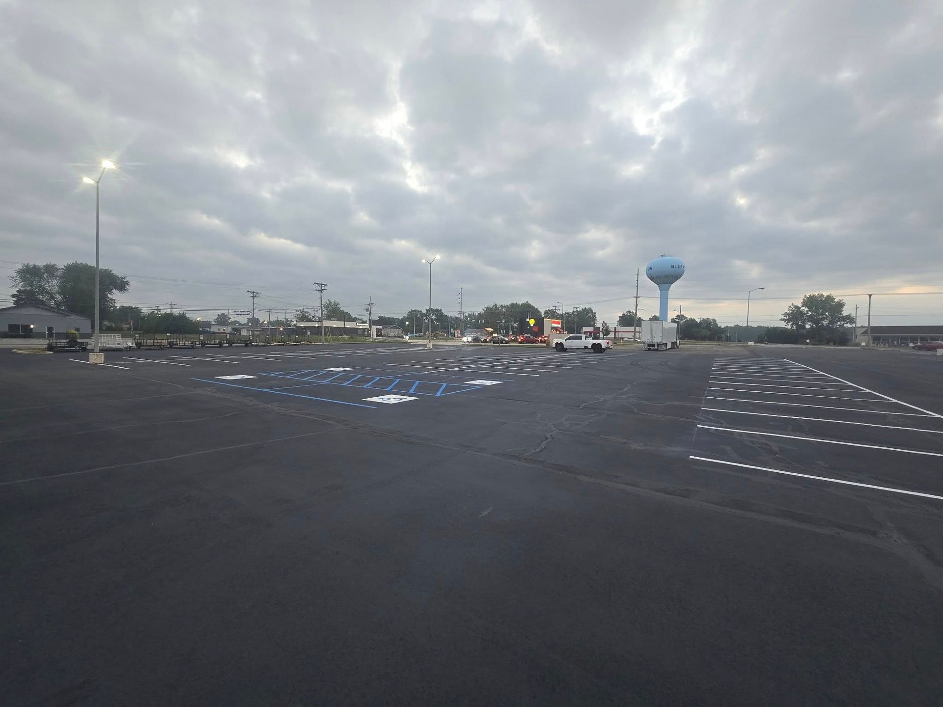 Empty parking lot under cloudy sky with streetlights and a blue water tower in the distance