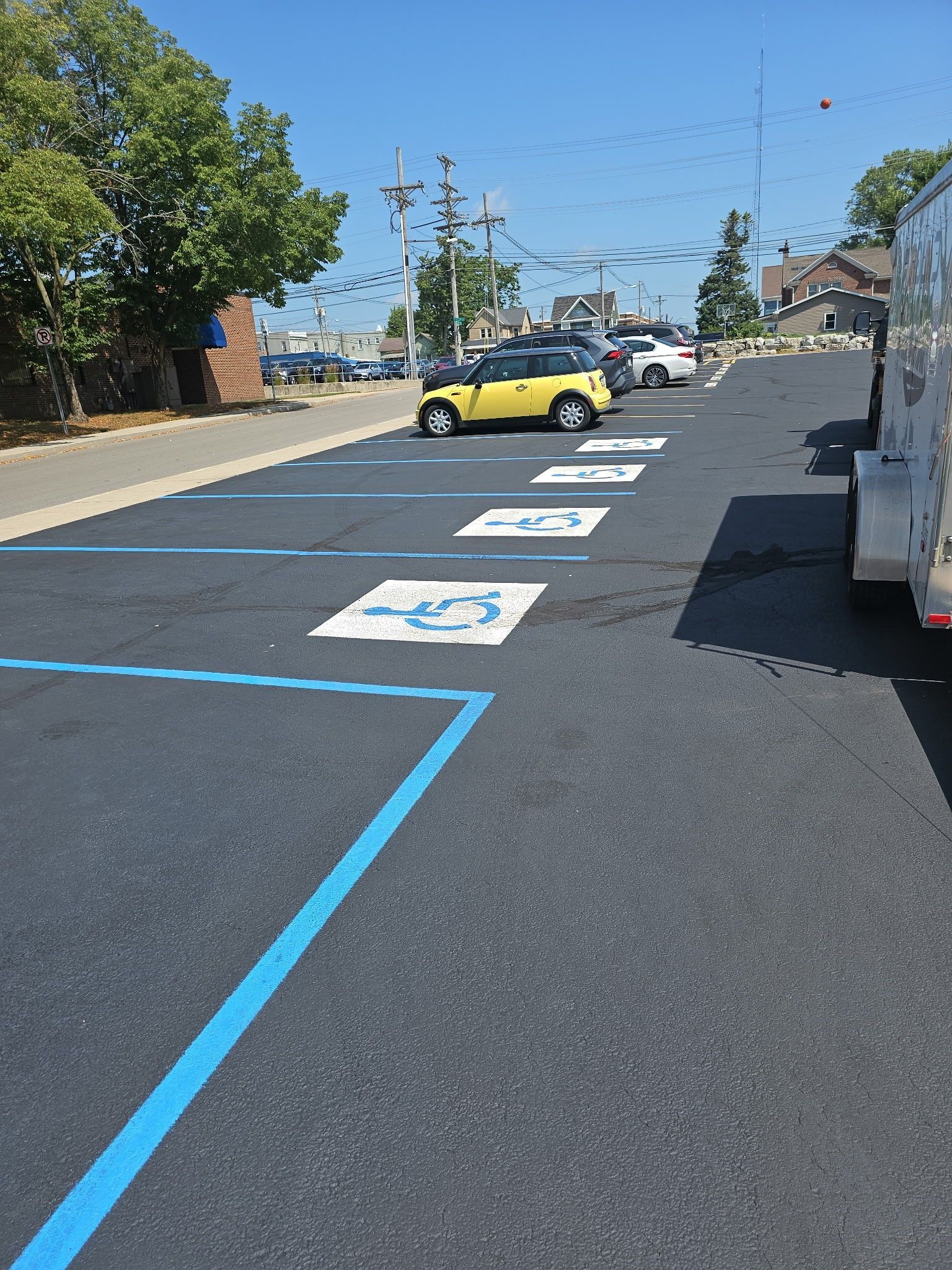 Accessible parking spaces painted on asphalt in a lot, with a yellow car and trees in the background