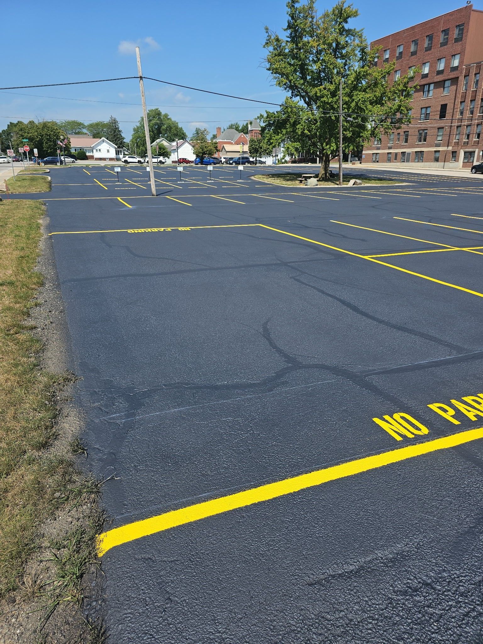 Empty parking lot with yellow painted parking lines on asphalt near brick buildings and trees.