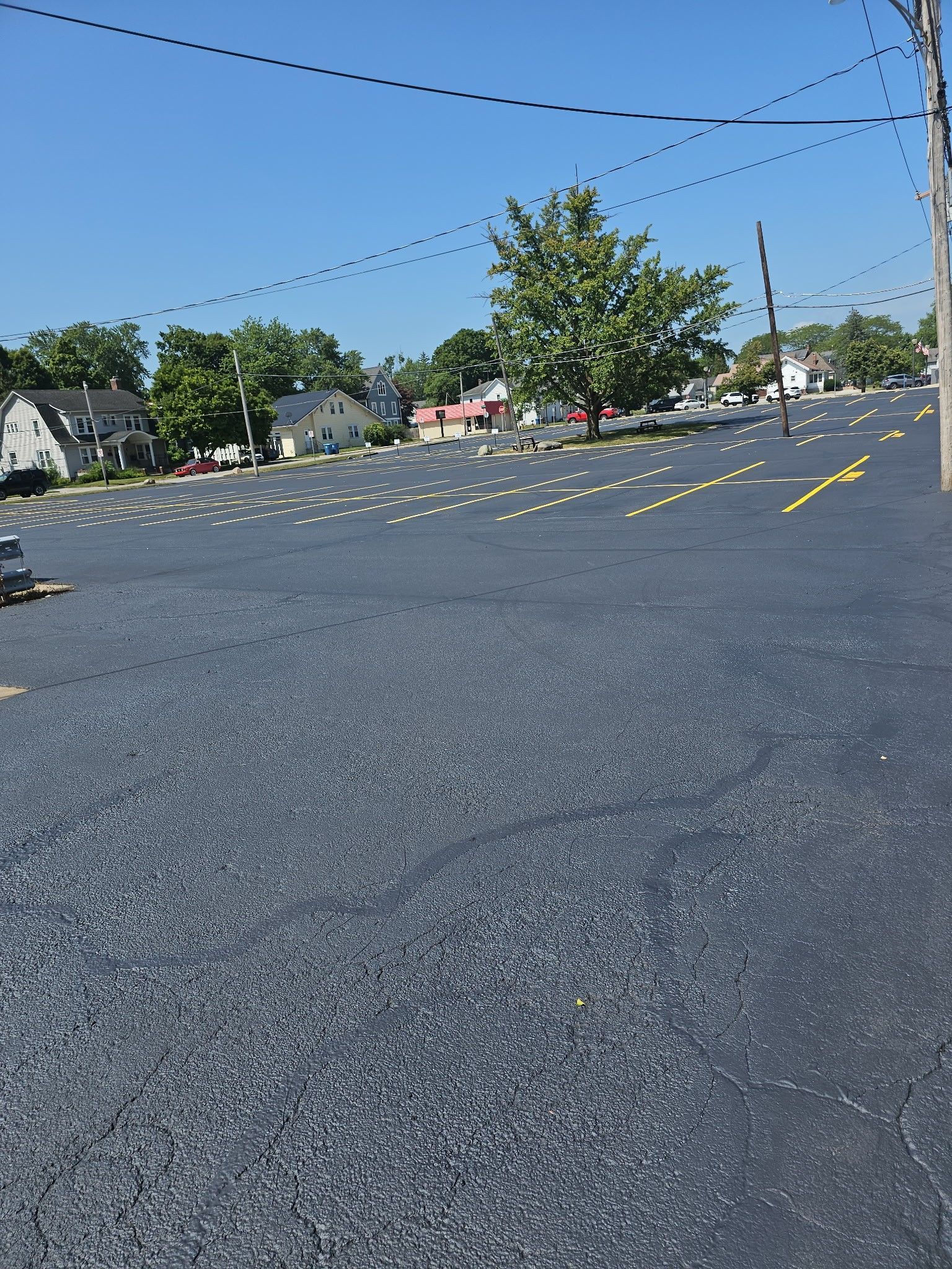 Empty parking lot with yellow lane markings and a tree under a clear blue sky.