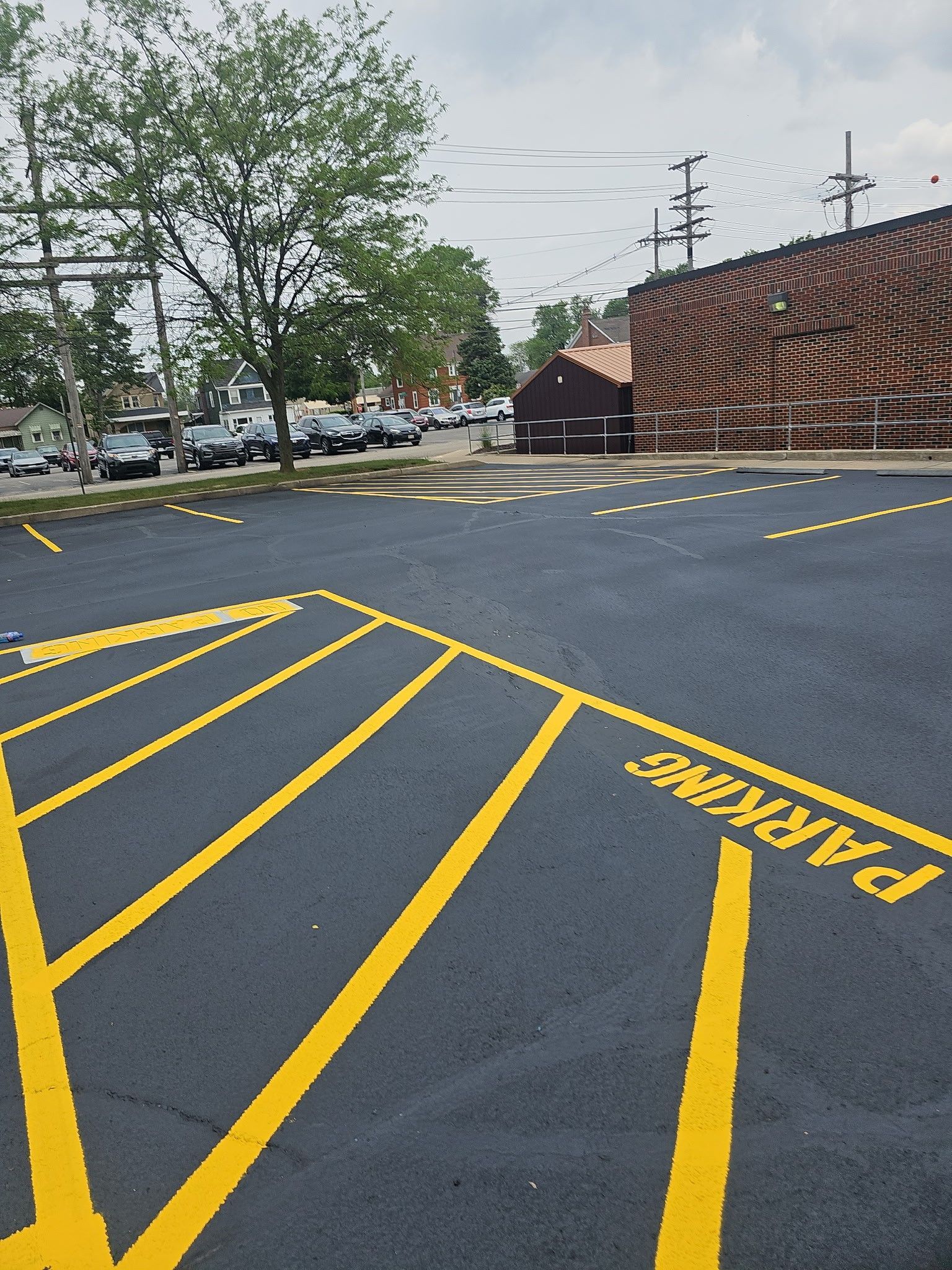 Empty parking lot with yellow diagonal no-parking lines and a brick building under overcast sky