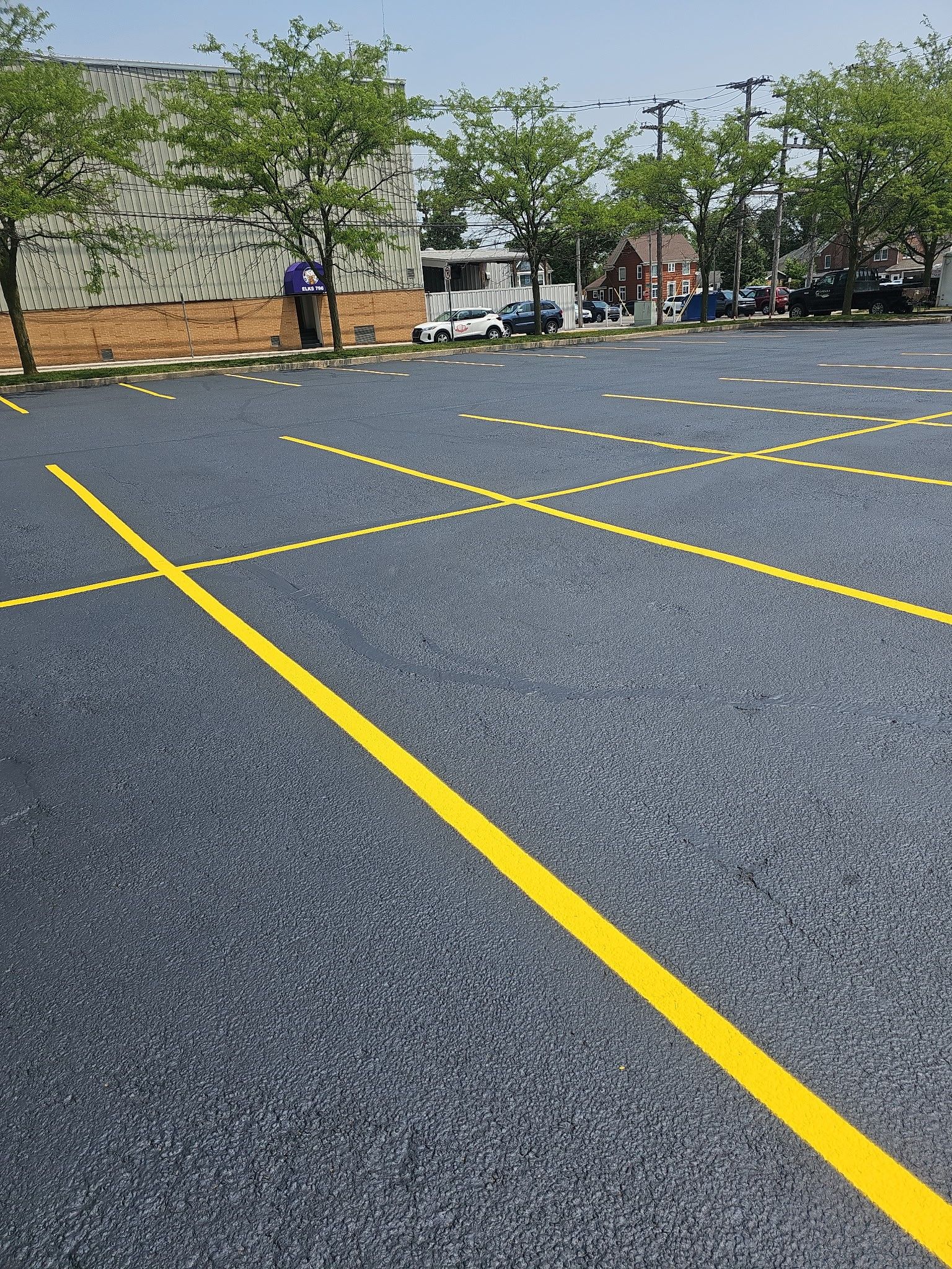 Empty outdoor parking lot with yellow lines, trees, and a few people near the far edge.