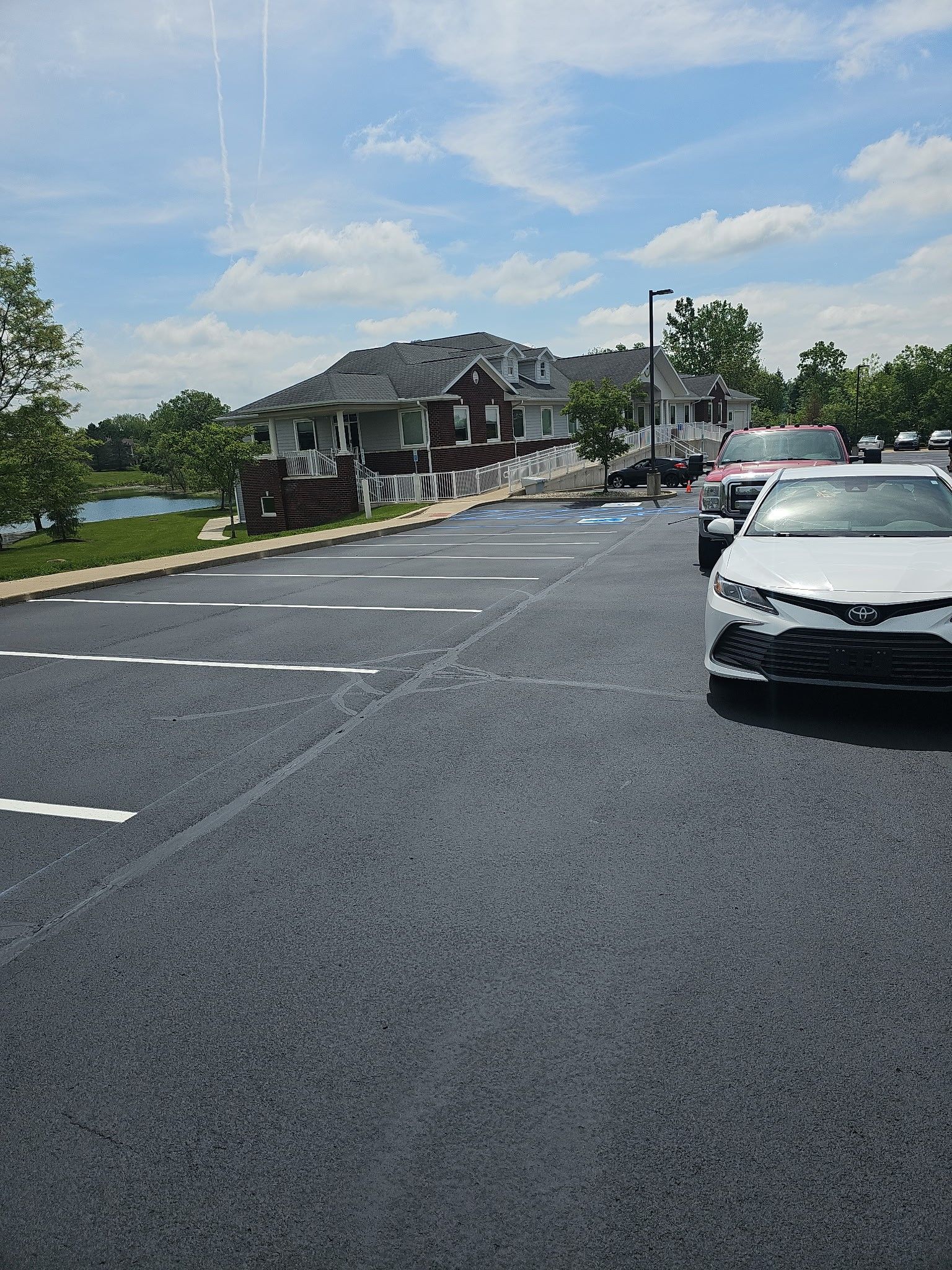 Parking lot with a black car, a building, and blue sky with clouds.