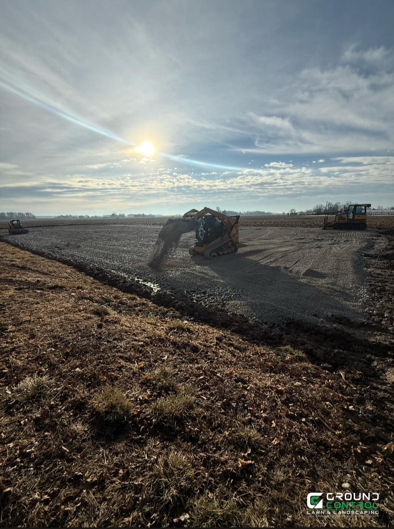 Bulldozer grading a gravel lot at sunset under a bright sky