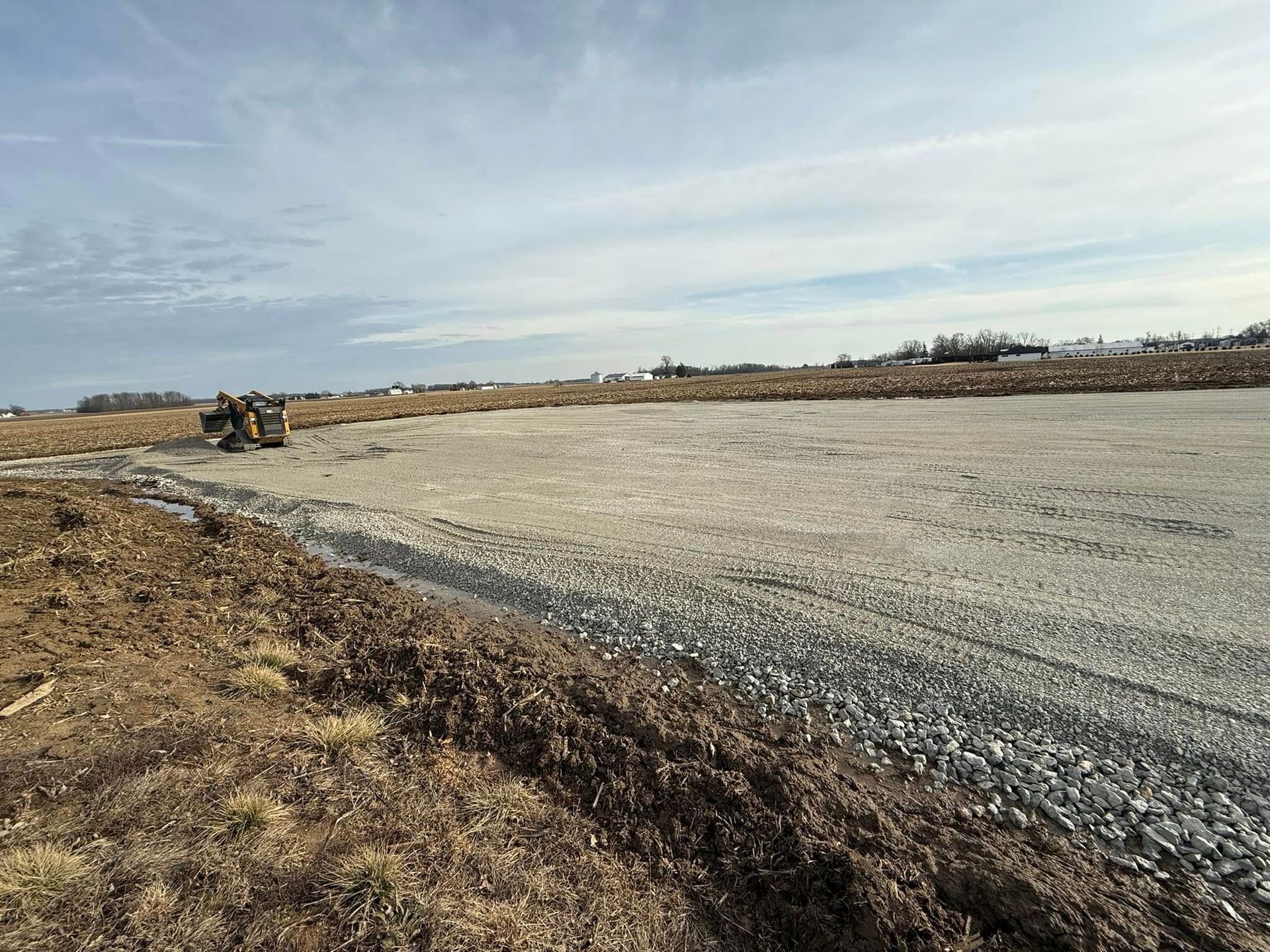 Gravel road under construction with an excavator on a barren, cloudy landscape