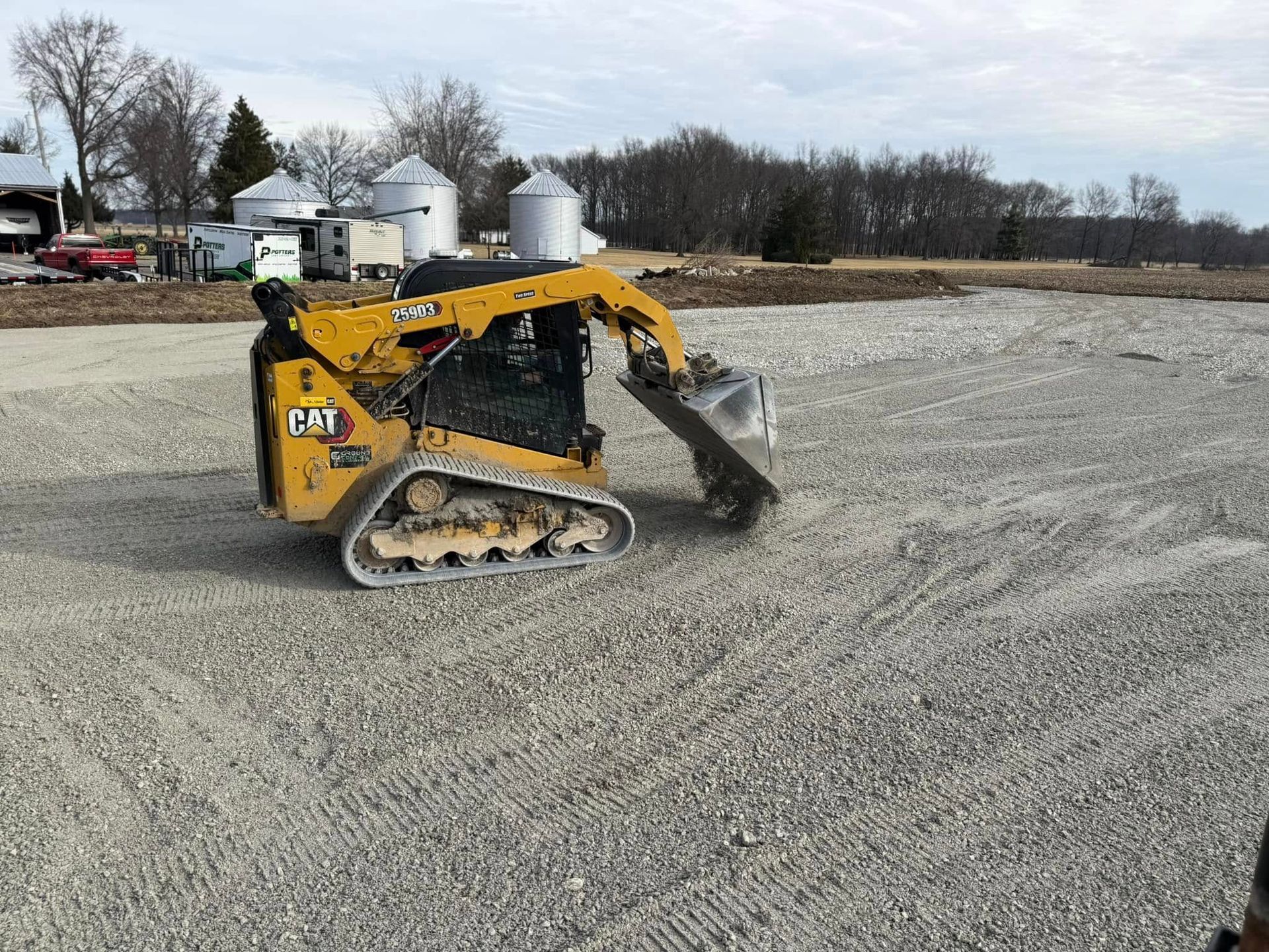 Yellow skid steer loader smoothing gravel in a wide open lot under a cloudy sky
