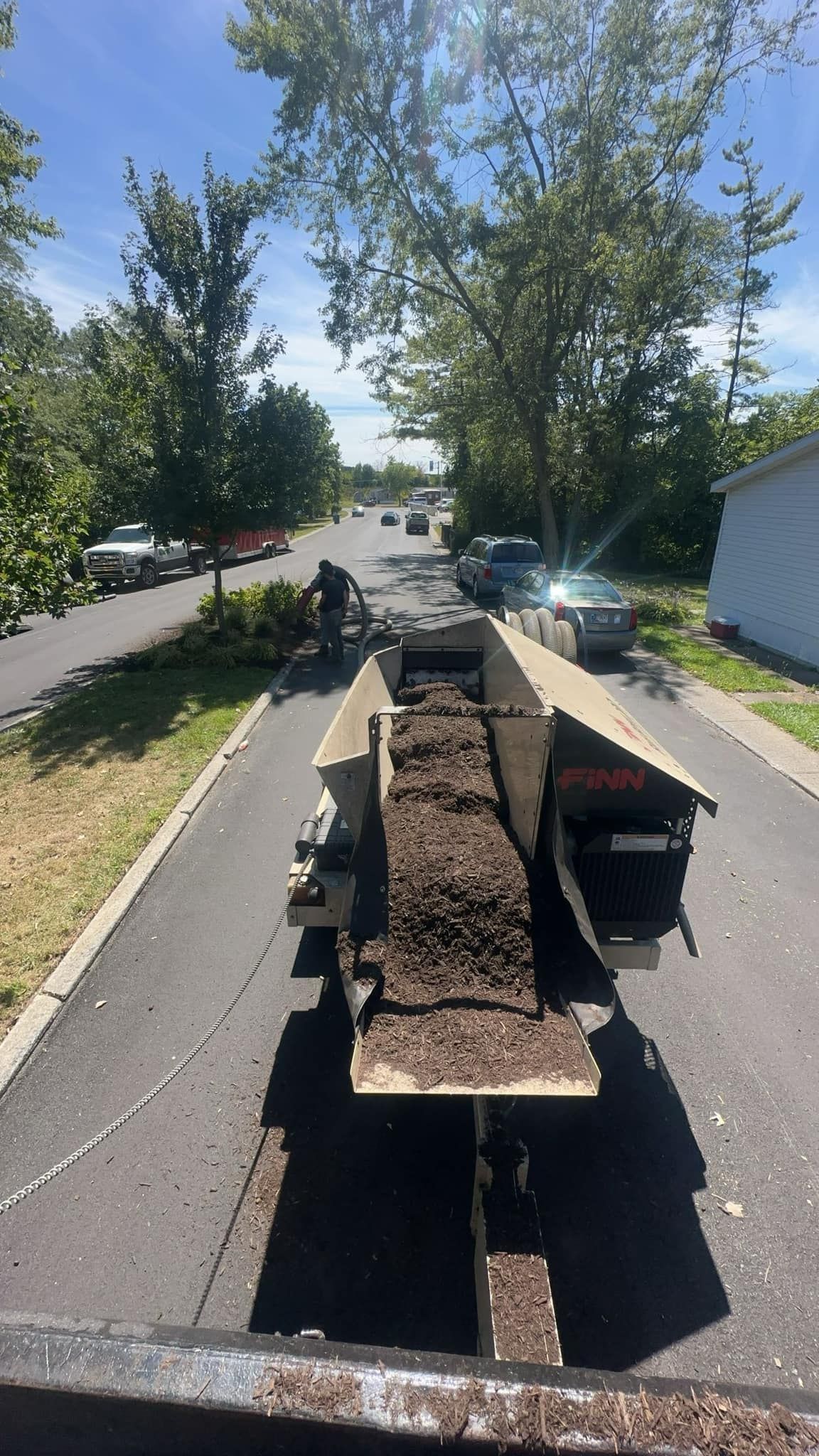 Dump truck hauling dirt along a tree-lined residential street on a sunny day