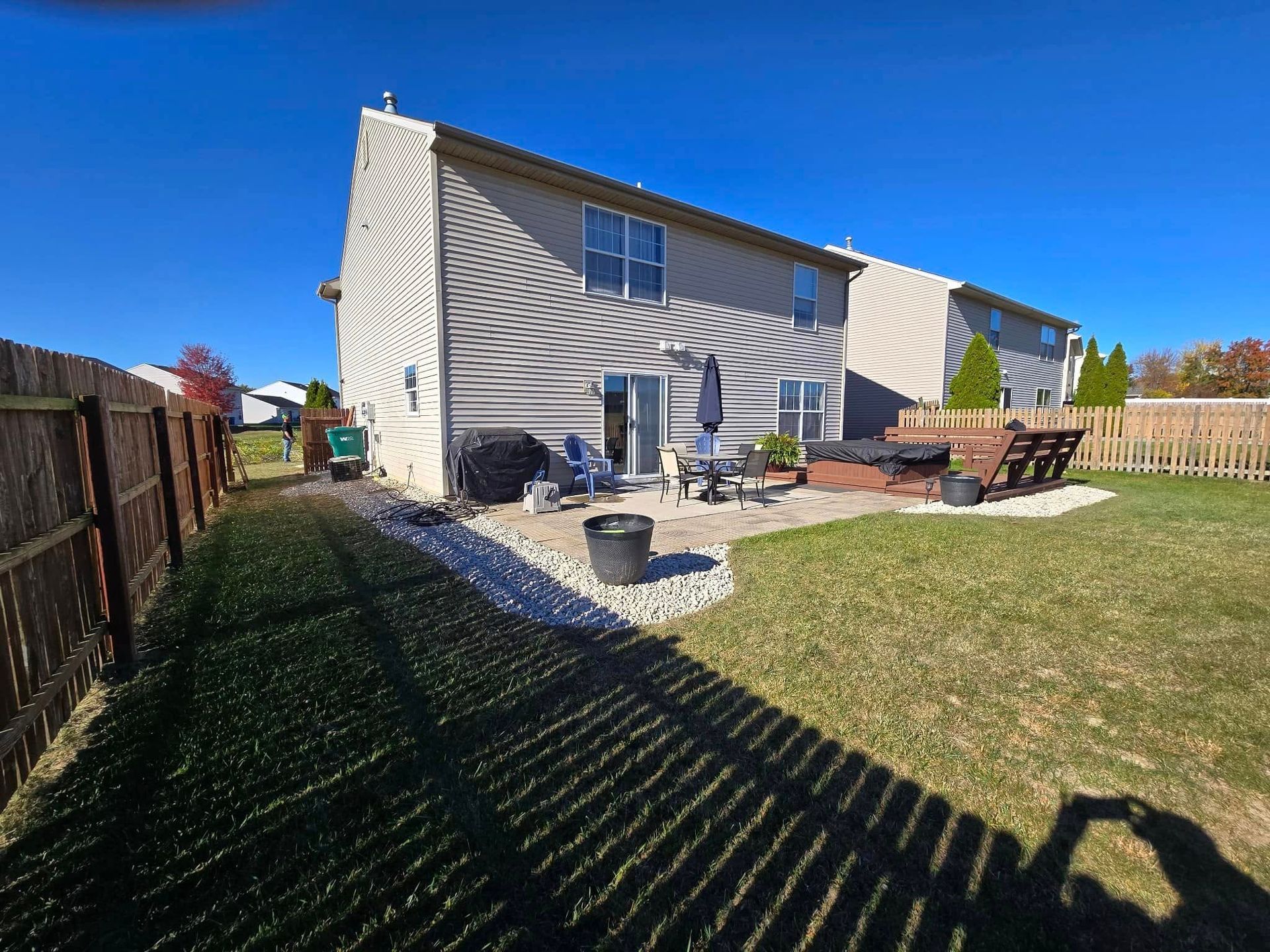 Backyard view of a house with patio furniture, fence, lawn, and long shadows in bright sunlight