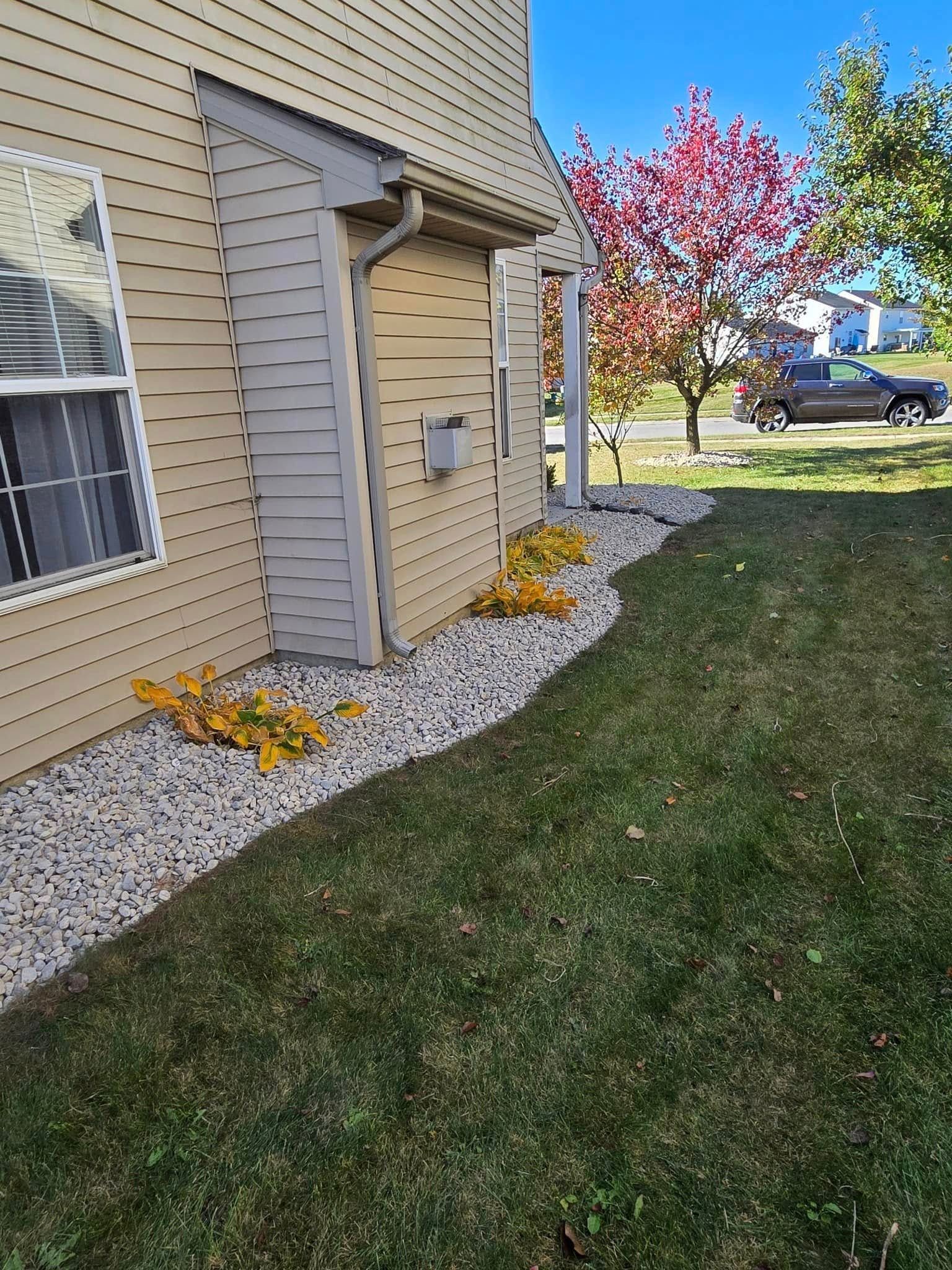 House exterior with beige siding, gravel bed, and a grassy lawn beside a flowering tree.