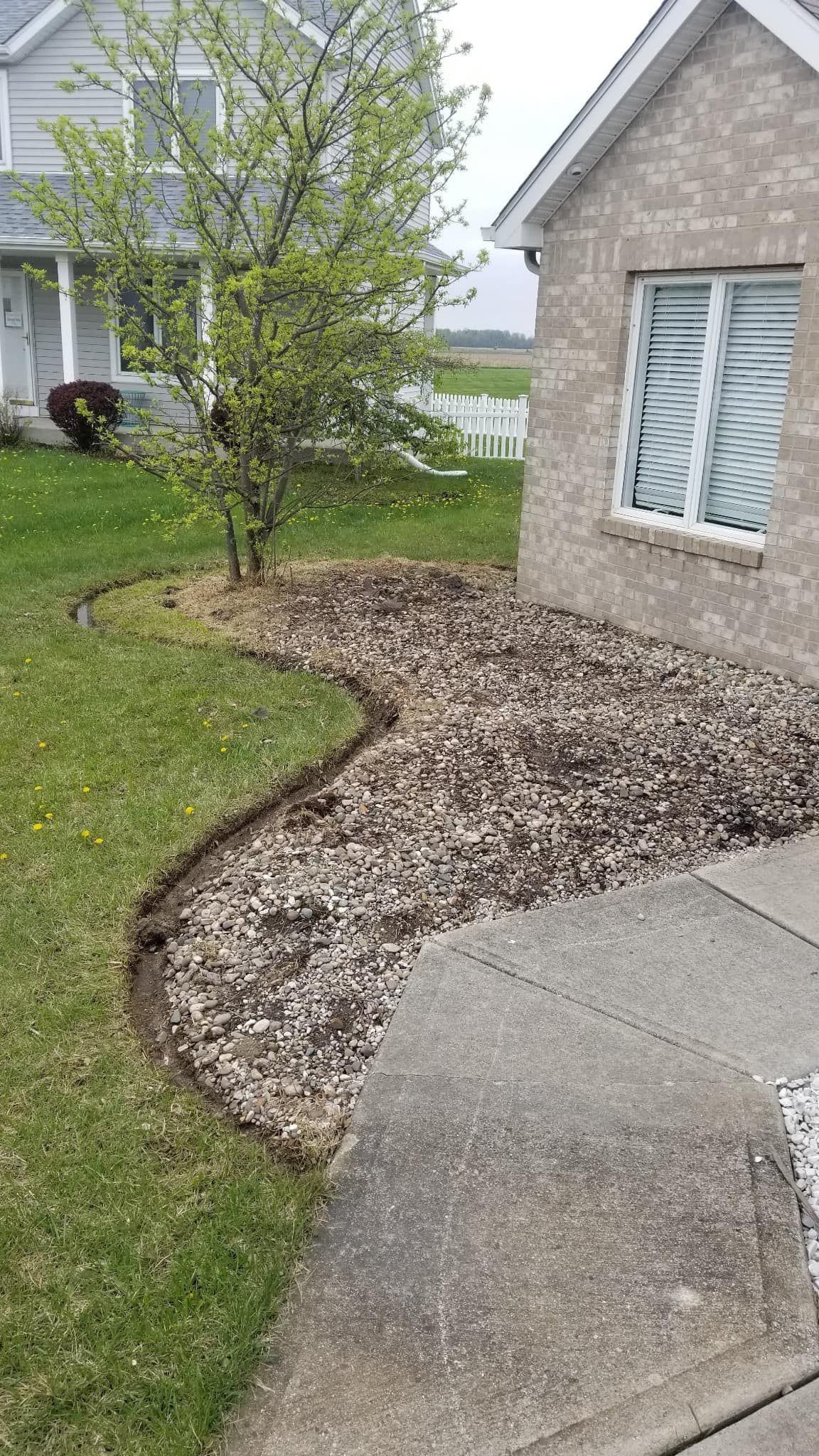 Curved concrete walkway beside a house, bordered by mulch and grass with a small tree.