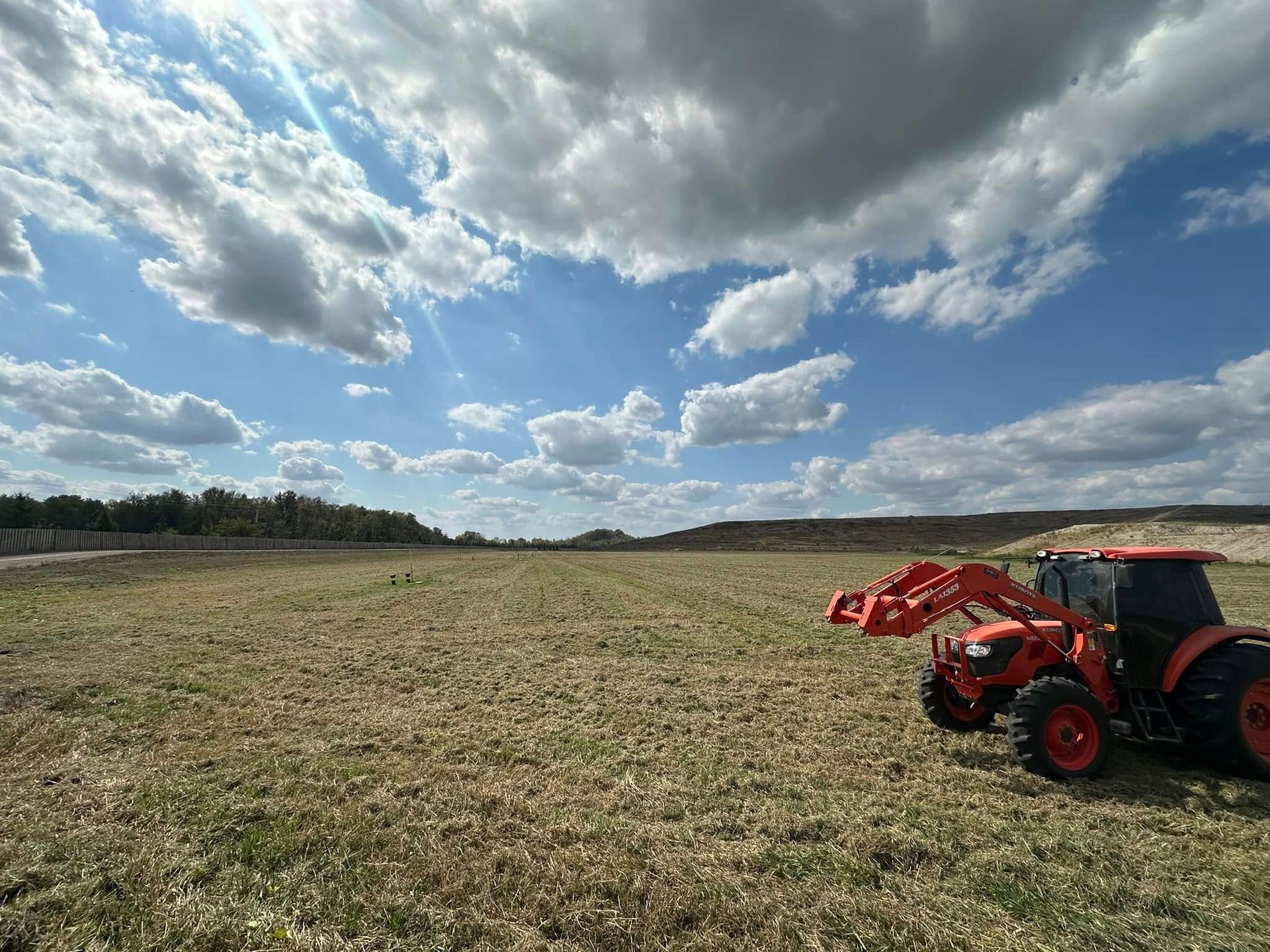 Red tractor in a harvested field under a cloudy blue sky