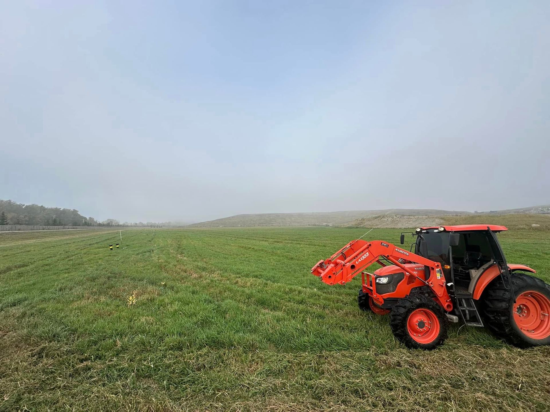 Red tractor in a green field under a cloudy sky, with plow attached on the right side.