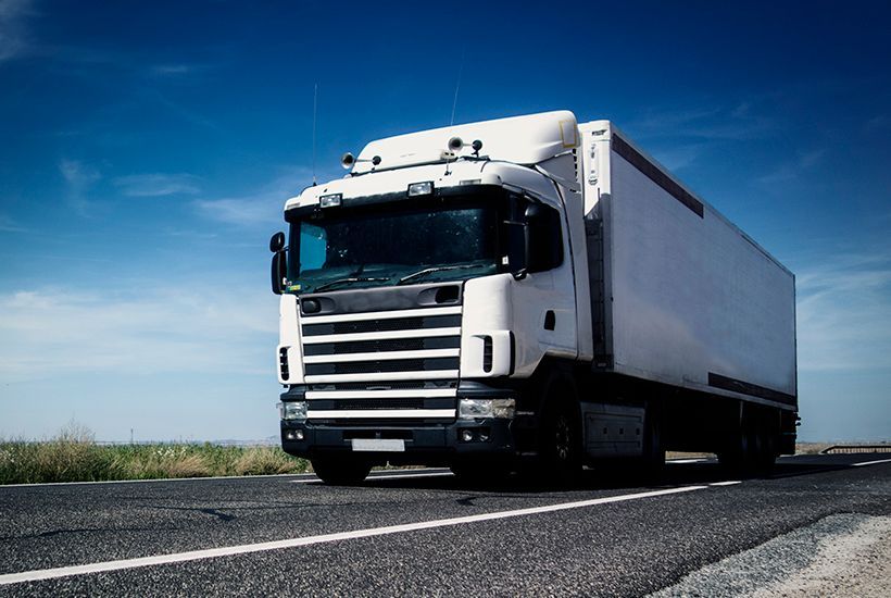White semi-truck driving on a road under a blue sky