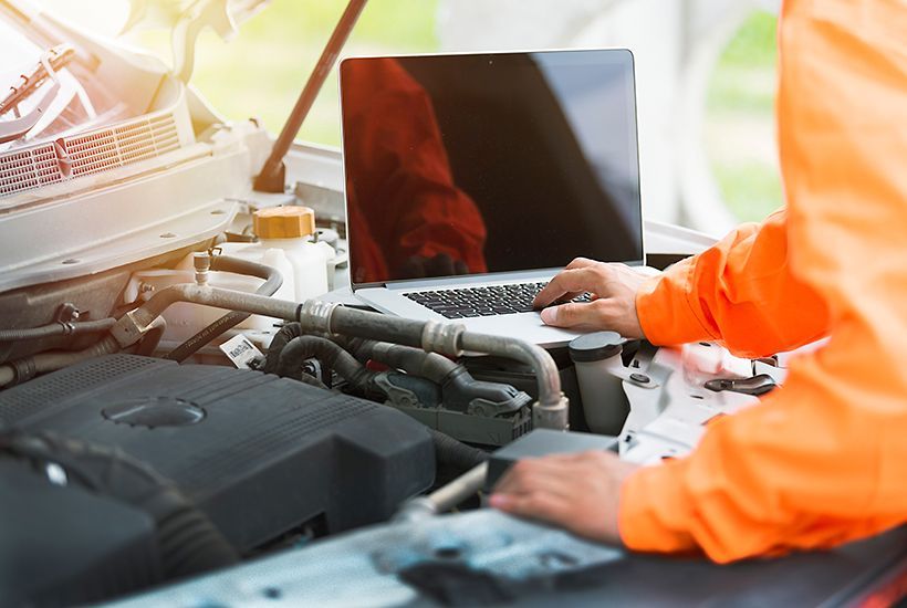 Mechanic in orange workwear inspecting a laptop beside an open car engine