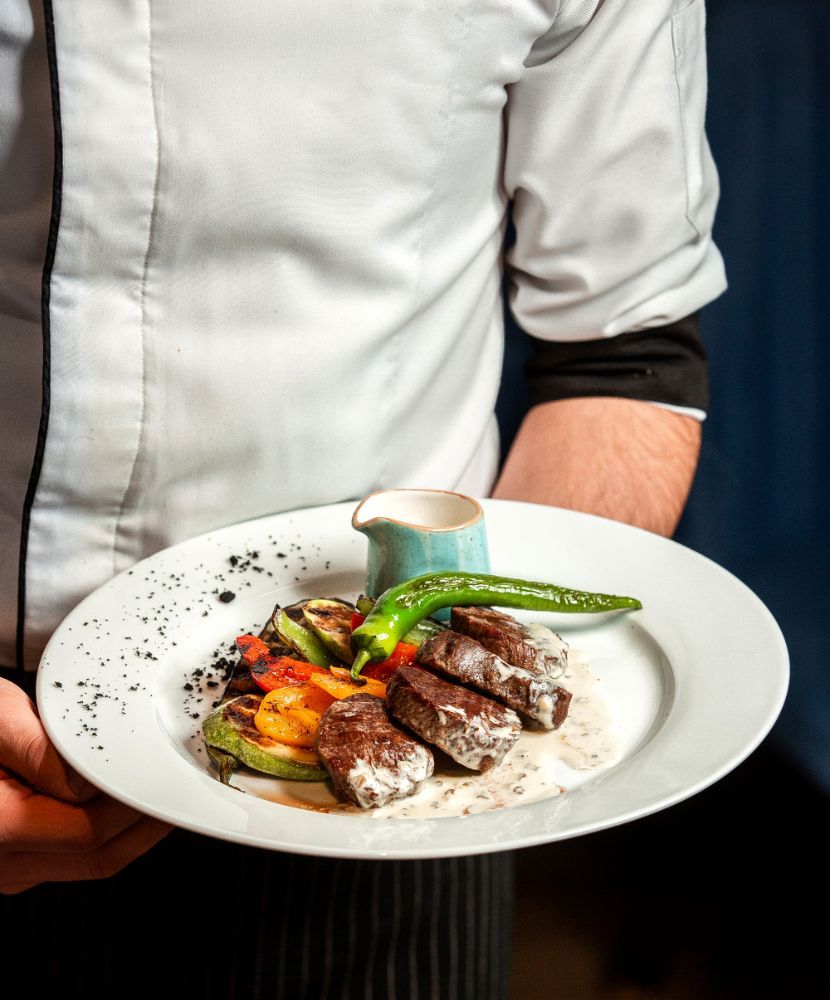 A chef is holding a plate of food with meat and vegetables.