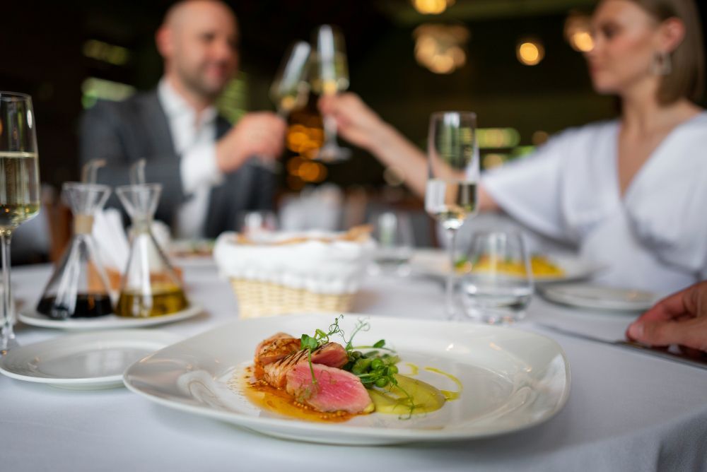 A man and a woman are sitting at a table with plates of food and glasses of wine.