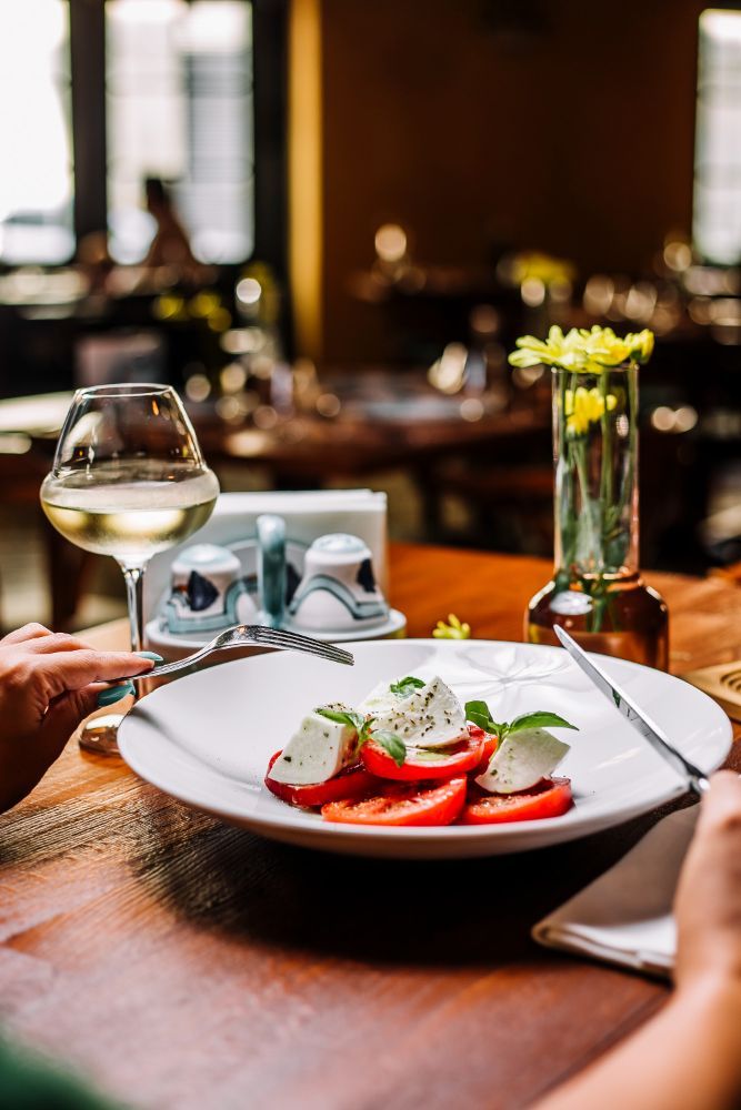 A person is sitting at a table with a plate of food and a glass of wine.