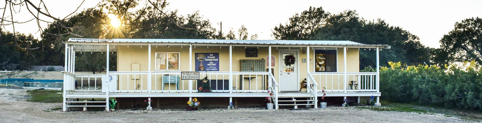 A yellow house with a white porch and trees in the background
