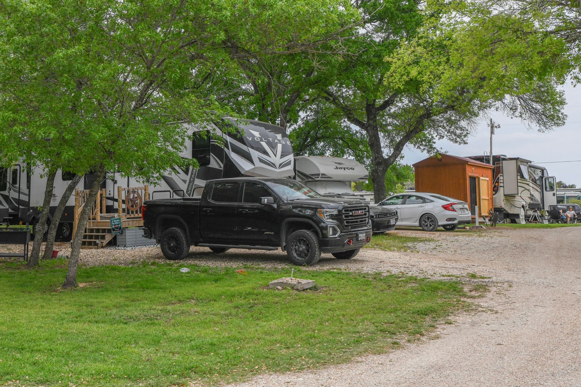 A black truck is parked in a grassy area next to a rv.