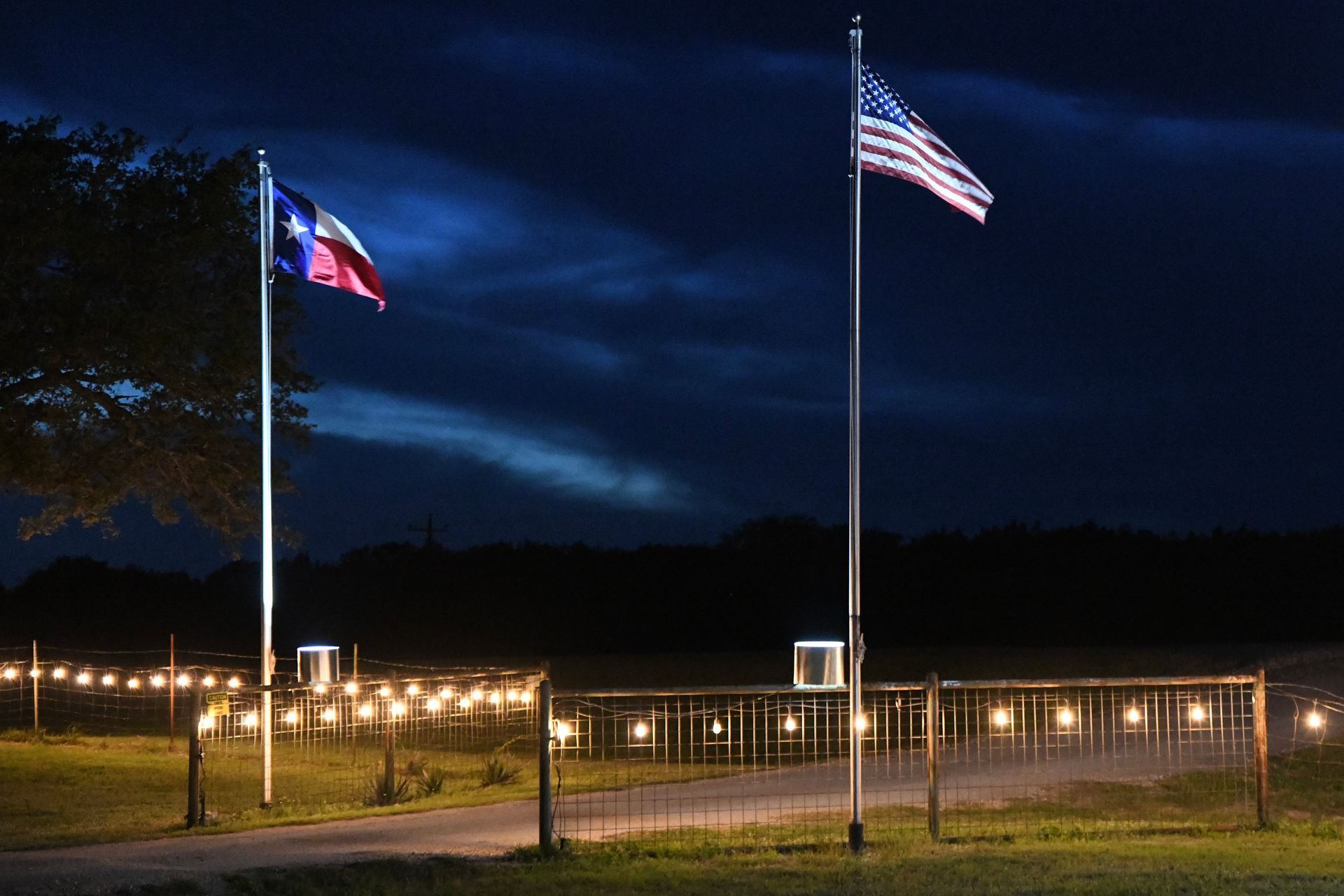 A texas flag and an american flag are flying in the wind at night.