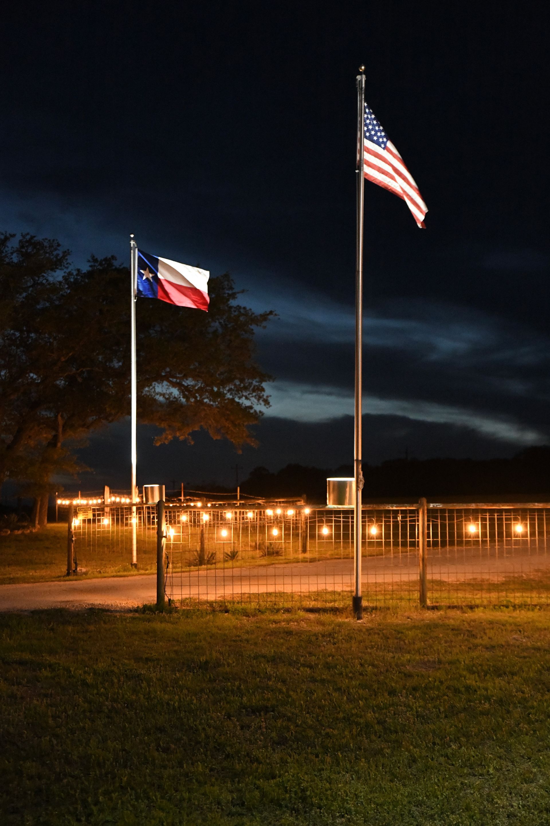 A texas flag and an american flag are flying in the wind at night.