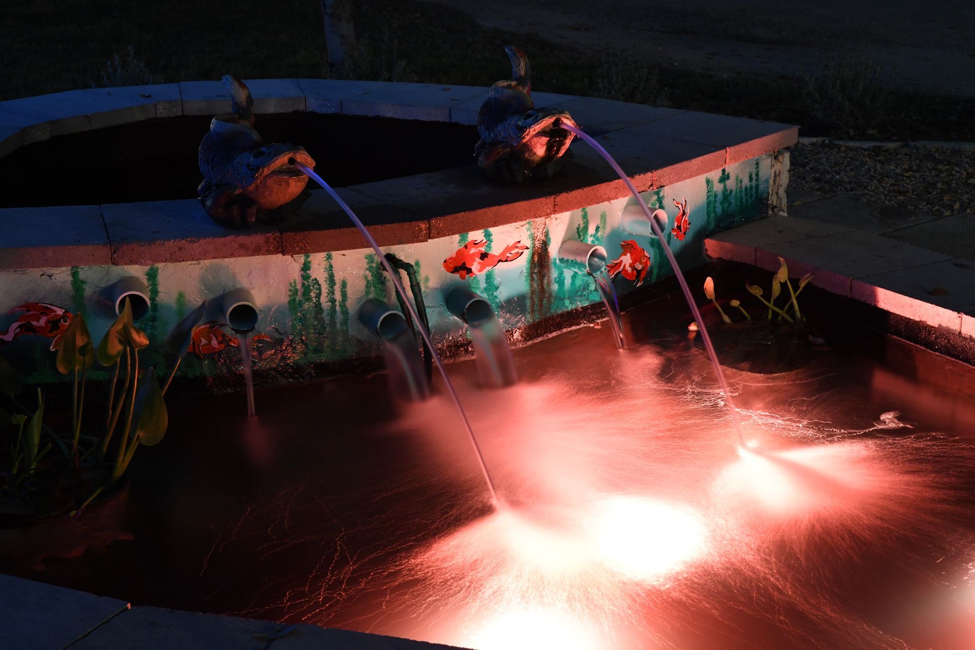 A fountain in the shape of a boat is lit up at night.