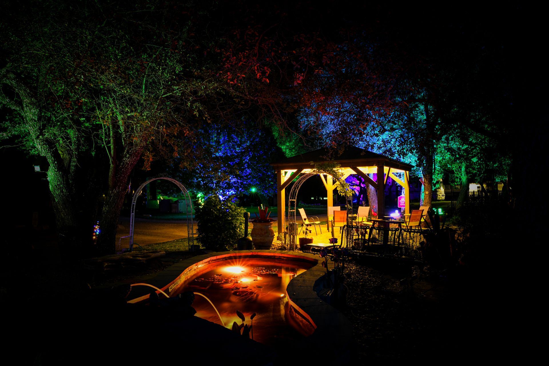 A gazebo is lit up at night with colorful lights surrounding it.