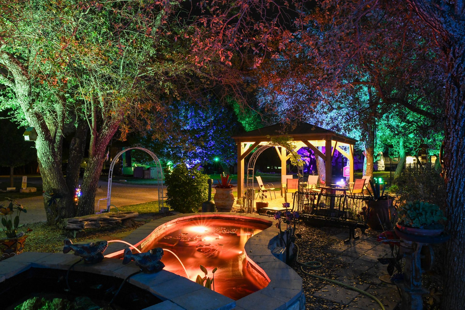 A gazebo is lit up at night with a pond in the foreground.