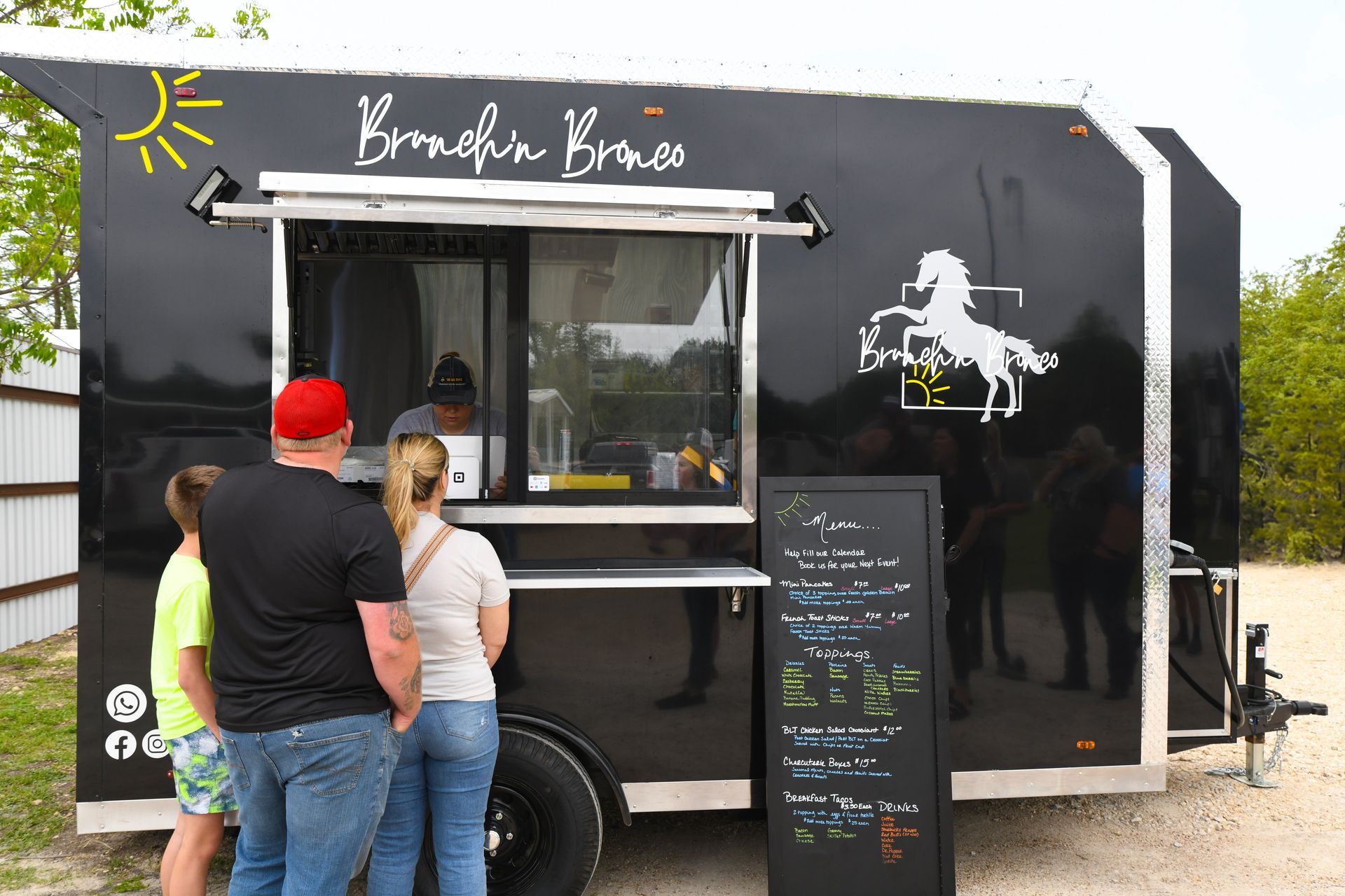 A group of people are standing in front of a black food truck.