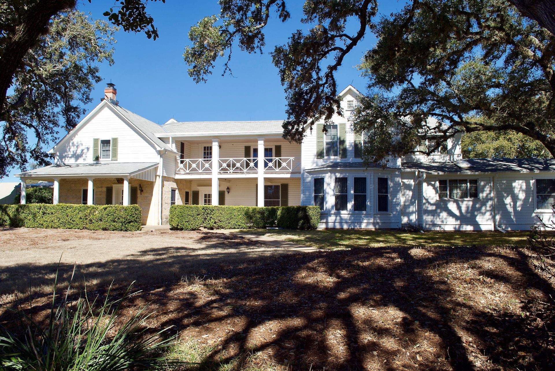 A large white house with a large porch is surrounded by trees