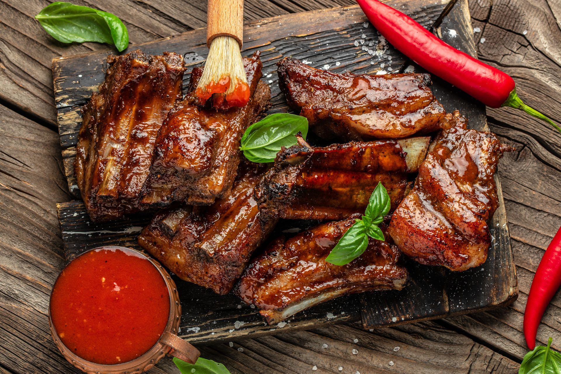 Ribs are being brushed with sauce on a wooden cutting board.