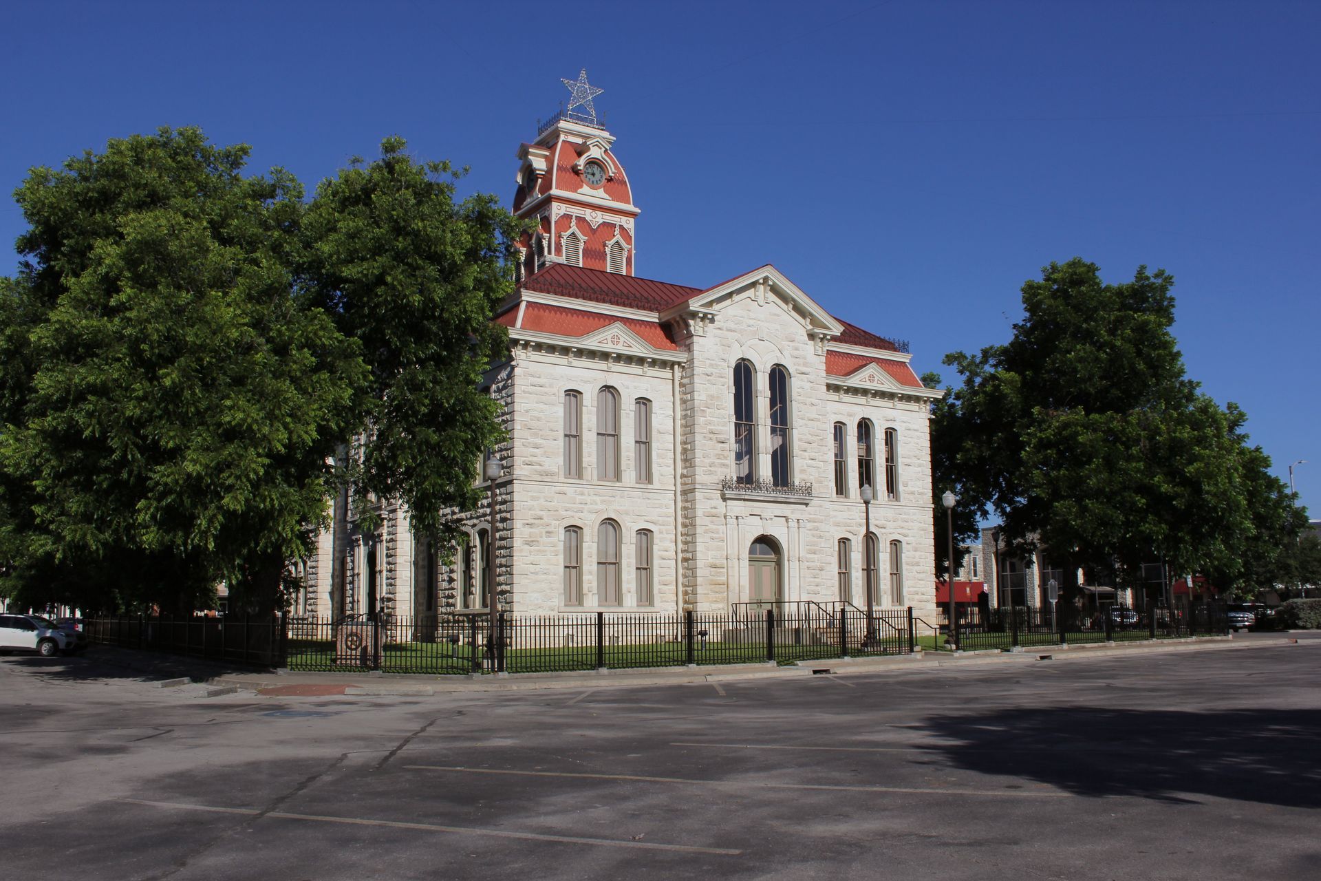 Historic limestone courthouse with red roof and tower, trees, and clear blue sky.
